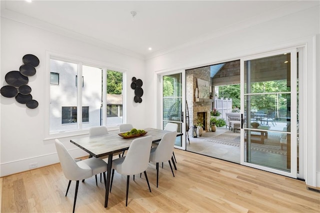 dining room with a large fireplace, light hardwood / wood-style floors, and crown molding