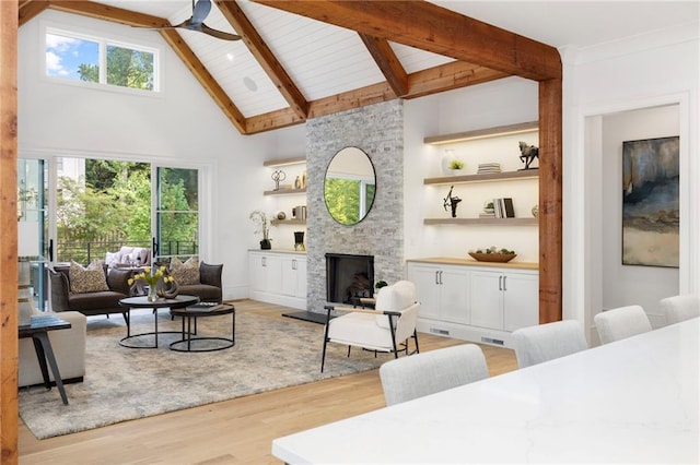 living room with ceiling fan, beam ceiling, high vaulted ceiling, light hardwood / wood-style floors, and a stone fireplace