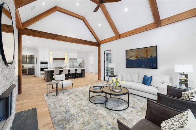 living room featuring beamed ceiling, light wood-type flooring, high vaulted ceiling, and ceiling fan