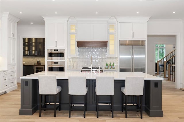 kitchen featuring white cabinets, crown molding, a large island with sink, and appliances with stainless steel finishes