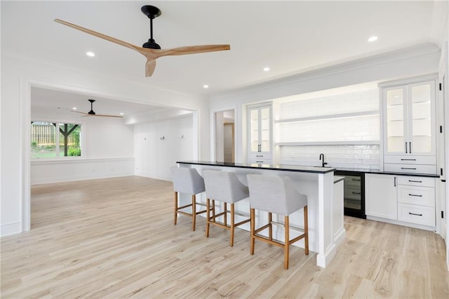 kitchen featuring ceiling fan, white cabinetry, light hardwood / wood-style floors, a kitchen island, and a breakfast bar area