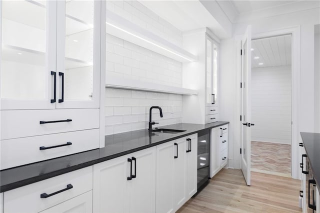 kitchen featuring sink, beverage cooler, tasteful backsplash, light hardwood / wood-style floors, and white cabinets