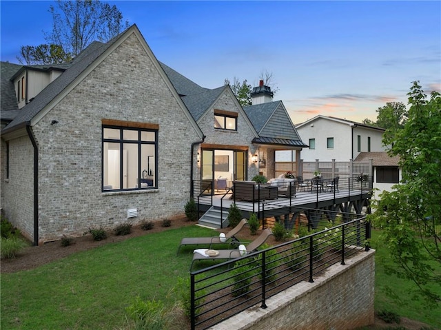 back house at dusk with a lawn, an outdoor living space, and a wooden deck