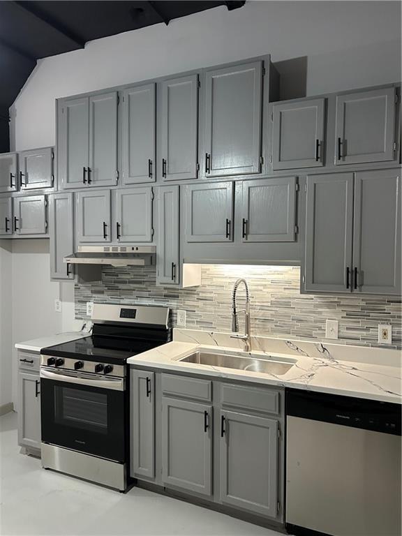 kitchen with sink, gray cabinets, stainless steel appliances, light stone countertops, and decorative backsplash