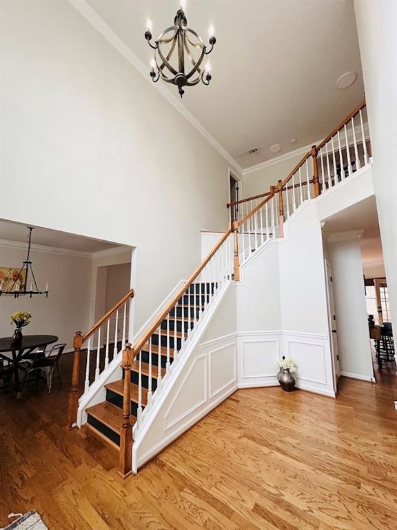 stairs with wainscoting, wood finished floors, an inviting chandelier, a high ceiling, and crown molding