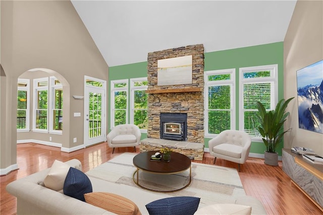 living room with arched walkways, a fireplace, wood finished floors, high vaulted ceiling, and baseboards