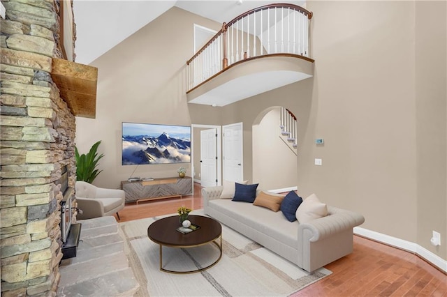 living room featuring arched walkways, baseboards, wood finished floors, a towering ceiling, and stairway