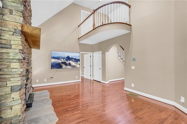 unfurnished living room with baseboards, arched walkways, a towering ceiling, and wood finished floors
