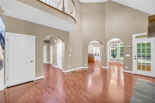 unfurnished living room featuring baseboards, arched walkways, a high ceiling, and wood finished floors
