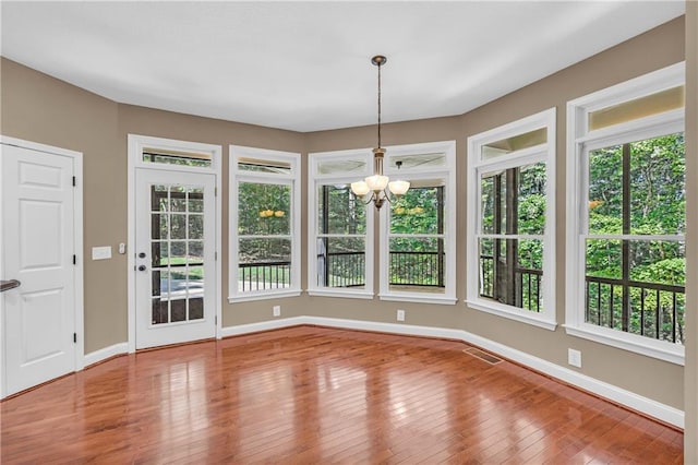 unfurnished dining area with baseboards, wood finished floors, a notable chandelier, and a wealth of natural light