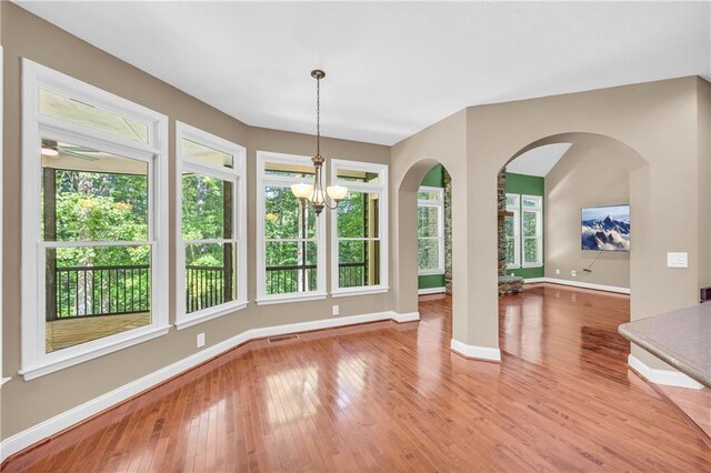 unfurnished dining area featuring a notable chandelier, light wood finished floors, arched walkways, baseboards, and visible vents