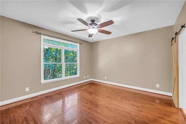 empty room featuring visible vents, baseboards, ceiling fan, a barn door, and hardwood / wood-style flooring