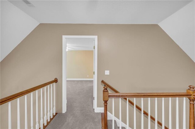 hall with visible vents, an upstairs landing, carpet, and vaulted ceiling