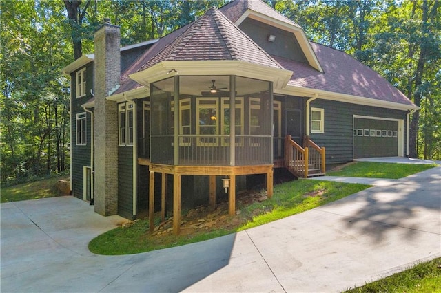 view of front of property with a shingled roof, a garage, a sunroom, a chimney, and concrete driveway