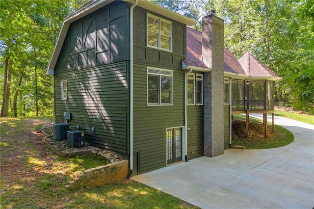 view of side of property featuring concrete driveway, a patio, a chimney, and cooling unit