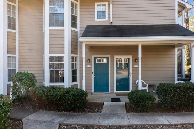 entrance to property with a shingled roof and a porch