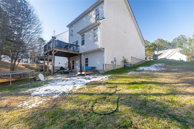 rear view of house with a wooden deck, a yard, and a trampoline