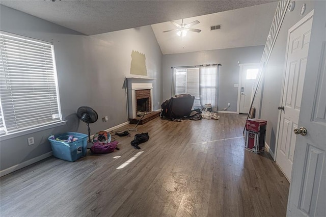 exercise area with lofted ceiling, ceiling fan, a fireplace, wood-type flooring, and a textured ceiling