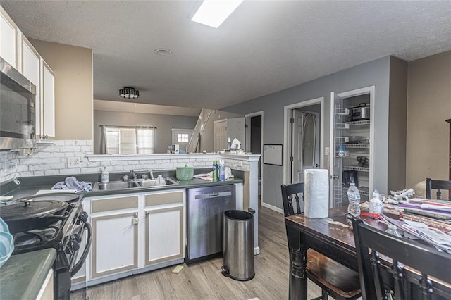 kitchen with appliances with stainless steel finishes, tasteful backsplash, white cabinetry, sink, and light hardwood / wood-style floors