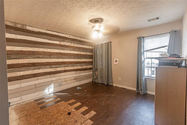 empty room with wooden walls, a textured ceiling, and plenty of natural light