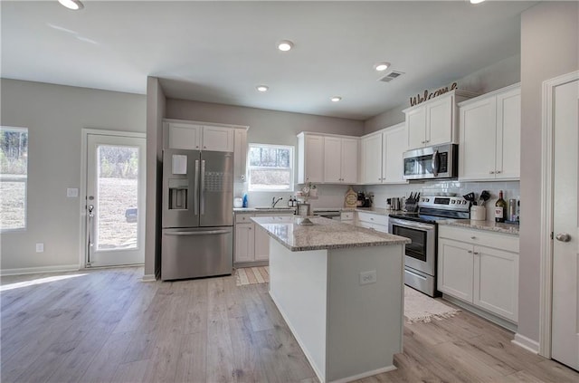 kitchen featuring stainless steel appliances, a center island, tasteful backsplash, light stone countertops, and white cabinets