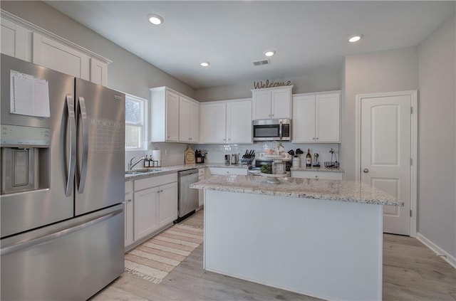 kitchen with white cabinetry, light stone counters, stainless steel appliances, and a kitchen island