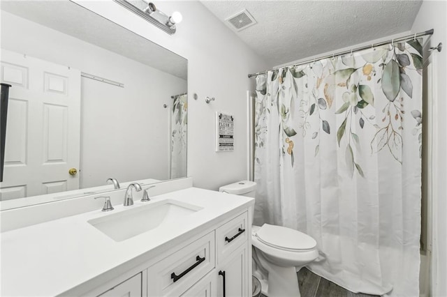 bathroom featuring visible vents, toilet, wood finished floors, a textured ceiling, and vanity