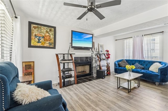 living room featuring a textured ceiling, a fireplace, baseboards, and wood finished floors