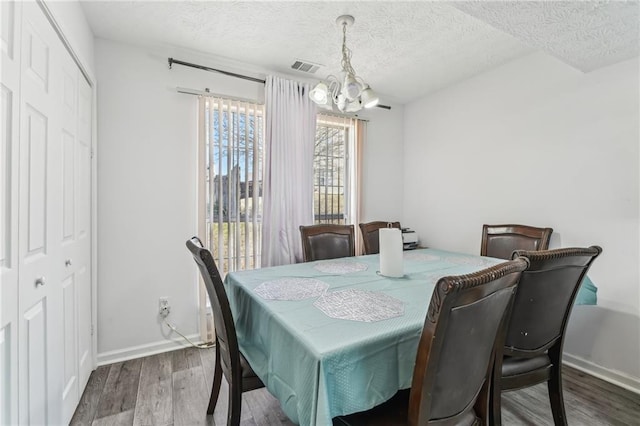 dining room featuring visible vents, a textured ceiling, wood finished floors, a chandelier, and baseboards