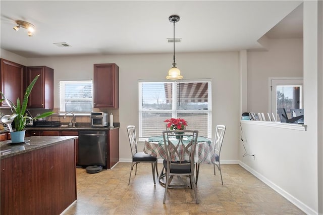 kitchen featuring stainless steel dishwasher, sink, dark stone countertops, and hanging light fixtures