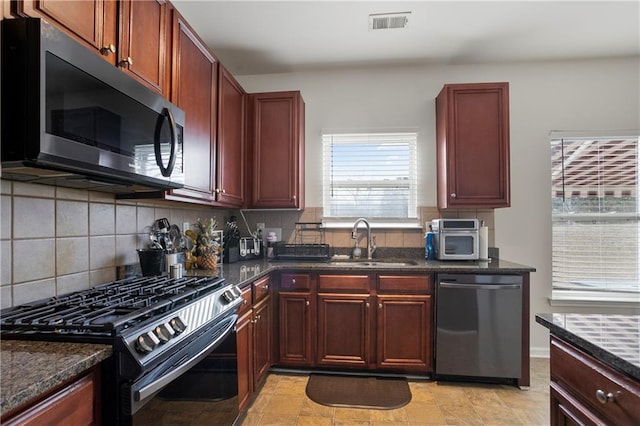 kitchen with tasteful backsplash, sink, dark stone counters, and stainless steel appliances