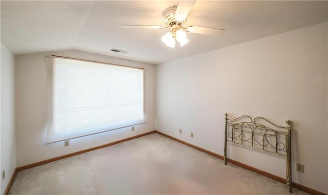 spare room featuring light colored carpet, visible vents, vaulted ceiling, ceiling fan, and baseboards