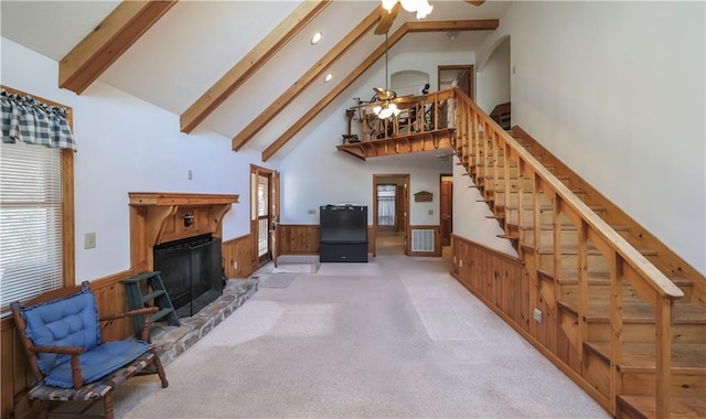 living room with beam ceiling, visible vents, a fireplace with raised hearth, wainscoting, and ceiling fan