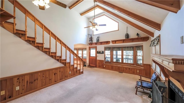 living area featuring a wainscoted wall, carpet floors, beamed ceiling, and stairs