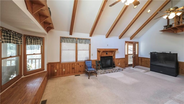 carpeted living area with a fireplace with raised hearth, high vaulted ceiling, a wainscoted wall, wood walls, and beamed ceiling