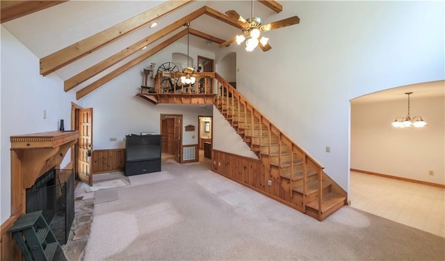 carpeted living area featuring stairway, a fireplace, high vaulted ceiling, beam ceiling, and ceiling fan with notable chandelier