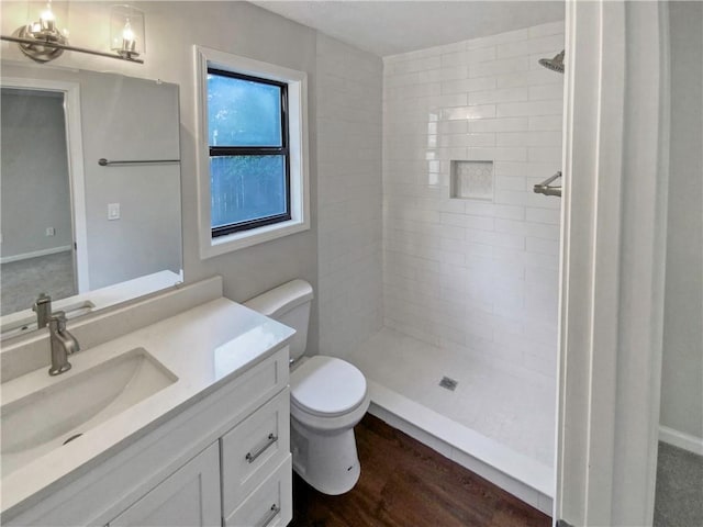 bathroom featuring a tile shower, vanity, wood-type flooring, and toilet