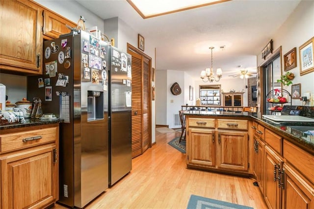 kitchen with a chandelier, dark stone countertops, stainless steel fridge, pendant lighting, and light hardwood / wood-style floors