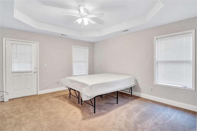 bedroom with a raised ceiling, ceiling fan, and light carpet