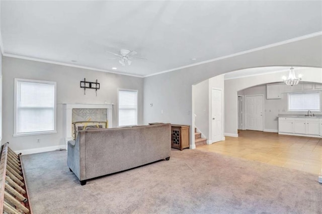 unfurnished living room with ceiling fan with notable chandelier, a high end fireplace, sink, light colored carpet, and crown molding