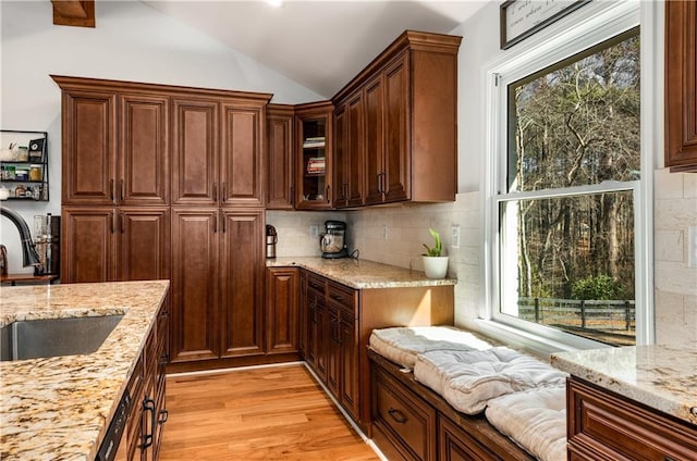 kitchen featuring sink, backsplash, light wood-type flooring, light stone counters, and lofted ceiling