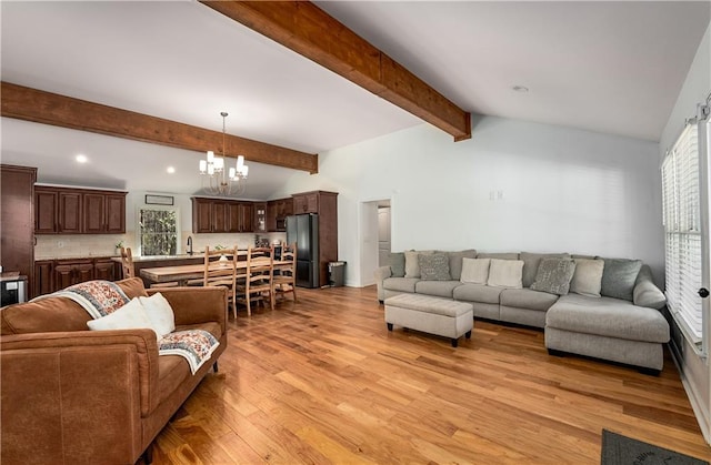 living room with a notable chandelier, light hardwood / wood-style flooring, a healthy amount of sunlight, and vaulted ceiling with beams