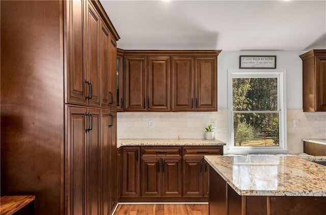 kitchen featuring backsplash, light wood-type flooring, and light stone counters