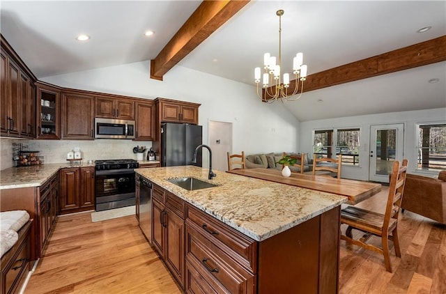 kitchen with sink, light hardwood / wood-style floors, vaulted ceiling with beams, an island with sink, and black appliances