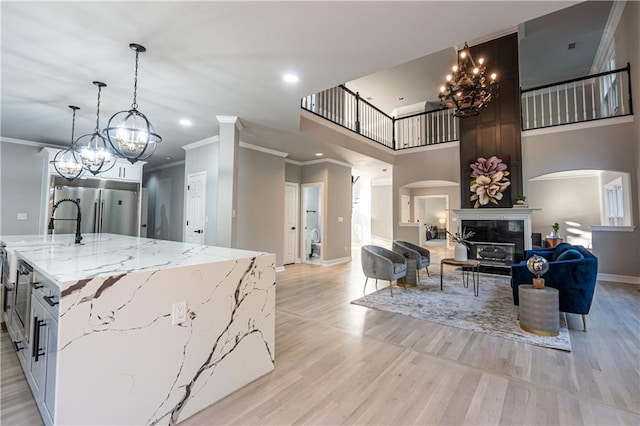 kitchen featuring a kitchen island with sink, open floor plan, light wood finished floors, stainless steel built in refrigerator, and a glass covered fireplace