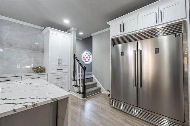 kitchen with crown molding, light wood-style flooring, white cabinets, light stone countertops, and stainless steel built in refrigerator