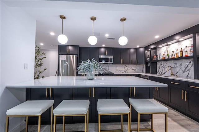 kitchen with light wood finished floors, a breakfast bar area, tasteful backsplash, hanging light fixtures, and appliances with stainless steel finishes