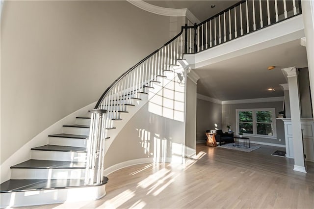 stairway with a high ceiling, baseboards, crown molding, and wood finished floors