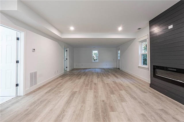 unfurnished living room featuring a large fireplace, light wood-type flooring, visible vents, and baseboards