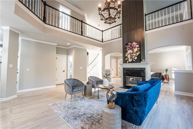 living room featuring light wood finished floors, baseboards, arched walkways, ornamental molding, and a fireplace